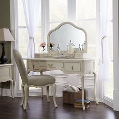 a white dressing table with a mirror, chair and vase on it in front of a window