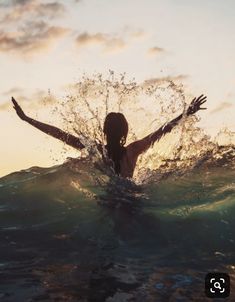 a woman standing in the water with her arms out and hands outstretched above her head