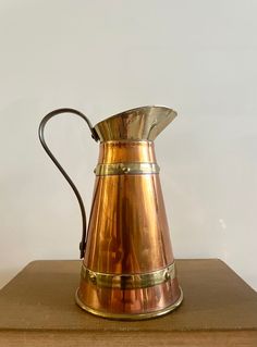 an antique brass pitcher sitting on top of a wooden table