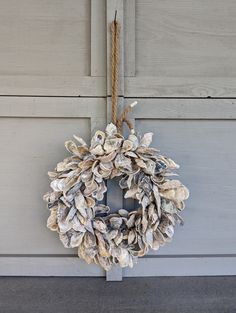 a wreath made out of seashells hanging on the side of a building with a rope