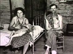 an old black and white photo of two people sitting on a bed in a room