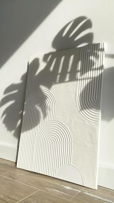 the shadow of a palm tree is cast on an art piece in front of a white wall