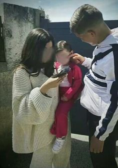 a woman holding a baby while another man combs it's hair in front of her