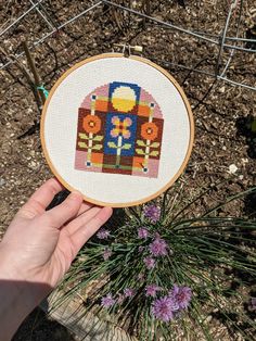 someone is holding up a cross - stitch pattern in front of some flowers and plants