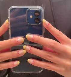 two hands with yellow and pink nail polish holding up a cell phone