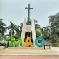 a large cross on top of a building next to stairs and palm trees in the background