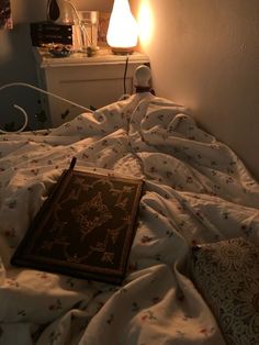 an open book sitting on top of a bed next to a night stand and lamp