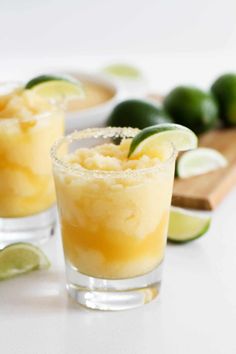 two glasses filled with pineapple margaritas next to limes