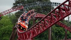 the roller coaster is red and has people riding on it, with trees in the background