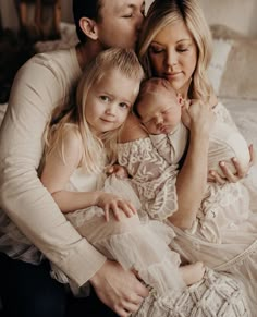 a woman, man and two children are sitting on a bed with their arms around each other