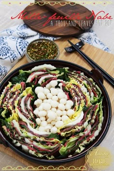 a salad is shown in a black bowl on a cutting board with chopsticks