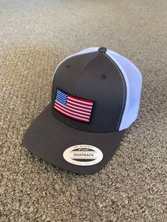 "This is a NEW United States of America Flag Embroidered Patch applied by hand to a high quality Yupoong or Richardson brand snapBack trucker hat Yupoong Classic SnapBacks are 65% Polyester/35% Cotton Structured 3 1/2\" mid-profile six-panel Permacurv Visor adjustable 6 7/8\" to 7 1/2\" Richardson Hats are 60% cotton/40% polyester Structured 3 1/2\" mid-profile six-panel Pre-curved Visor adjustable snapback closure 6 3/4\" -7 5/8\" Every Hat Design we offer is Created and Individually HANDCRAFTE Gray Trucker Hat One Size, Gray Trucker Cap, Country Style Snapback Hat With Curved Brim, Country Style White Baseball Cap, Country Style White Snapback Hat, Trucker Baseball Cap With Curved Brim Made In Usa, Country Style Adjustable Snapback Baseball Cap, Adjustable Country Style Snapback Baseball Cap, Adjustable Patriotic Hat For Outdoors