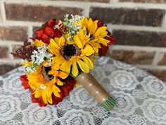 a bouquet of sunflowers and red roses sits on a lace covered tablecloth