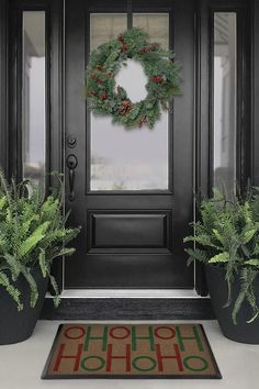 a black front door with two plants and a wreath on it