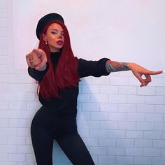 a woman with long red hair pointing at the camera while standing in front of a white brick wall