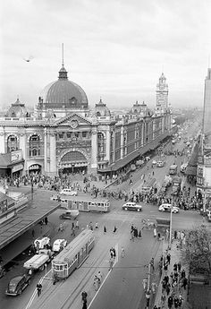 black and white photograph of an old city street with buses, cars, and pedestrians