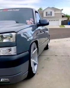 the front end of a blue truck parked on top of a driveway next to a house