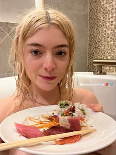 a woman sitting in a bathtub holding a plate with sushi and chopsticks