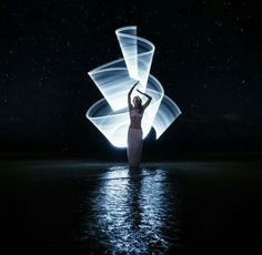 a woman is standing in the water with her arms up and lights projected on her body