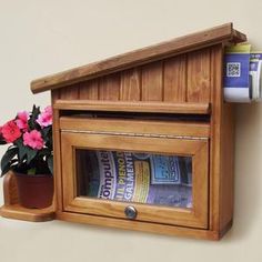 a wooden mailbox with money in it next to a potted plant on the wall