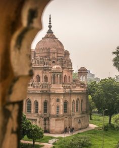 an old building in the middle of a lush green park with people walking around it