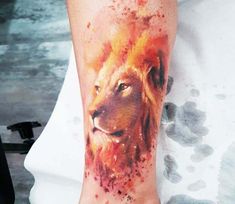 a lion tattoo on the ankle with watercolor paint splatters all over it