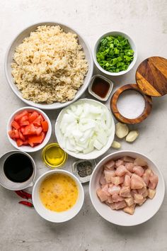 an overhead view of various ingredients in small bowls on a white countertop, including rice, chicken, and vegetables