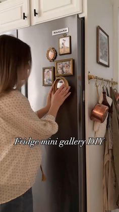 a woman is looking at pictures on the wall in front of her refrigerator and touching it with her hand