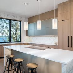 a kitchen with marble counter tops and stools next to an island in front of a large window