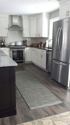 a kitchen with stainless steel appliances and white cabinets, hardwood floors, and gray rugs