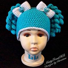 a crocheted blue hat with white bows on the top and ears is shown in front of a mannequin's head