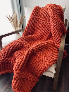 an orange knitted blanket sitting on top of a wooden chair