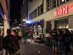 people are standing on the sidewalk in front of a kon - t store at night