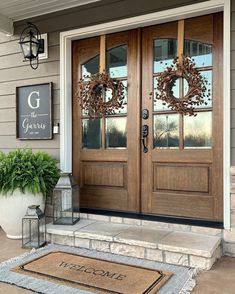 a front door with two wreaths on it and a welcome mat that says g