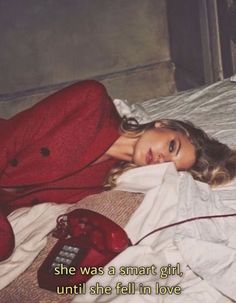 a woman laying on top of a bed next to a red phone and telephone cord