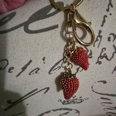 two strawberries are attached to a gold keychain on top of a fabric