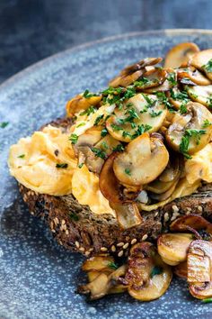 an open face sandwich topped with mushrooms and chives on a blue plate that says, creamy scrambled eggs with mushrooms