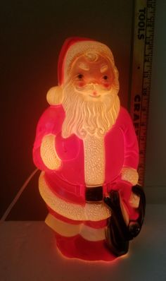 a light up santa clause holding a black bag with a measuring tape behind it on a table