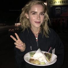 a woman holding a plate with food on it in front of a building at night