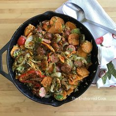 a skillet filled with meat and vegetables on top of a wooden table next to a white towel