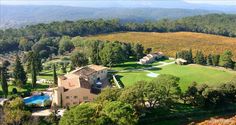 an aerial view of a large house surrounded by trees and hills with a pool in the middle