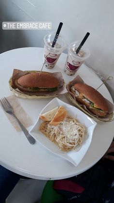 two sandwiches and spaghetti on a white plate with silverware next to eachother