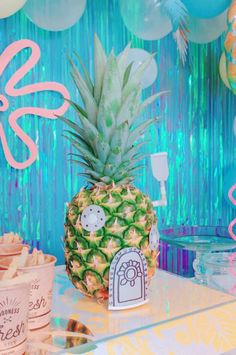 a pineapple sitting on top of a table in front of balloons and streamers