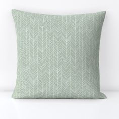 a light green pillow with white leaves on the front and back, sitting on a white surface