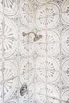 the shower head is attached to the wall with an intricate pattern on it's tile