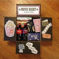 an open box filled with movies and sodas on top of a wooden table next to a movie ticket