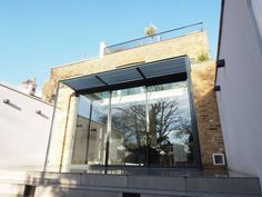 an outside view of a building with glass walls and trees on the roof, in front of a brick wall