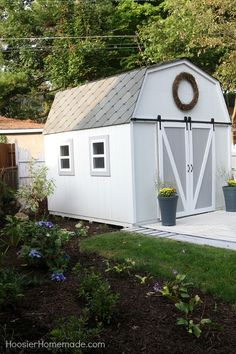 a white shed with a wreath on the door and flowers in pots next to it