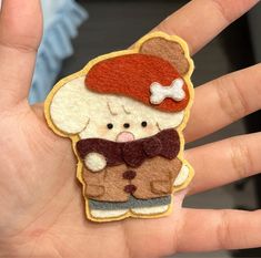 a hand holding a small patch with a bear wearing a red hat and bow tie