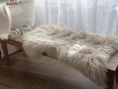 a bench with a fur rug on it in front of a white curtain and window